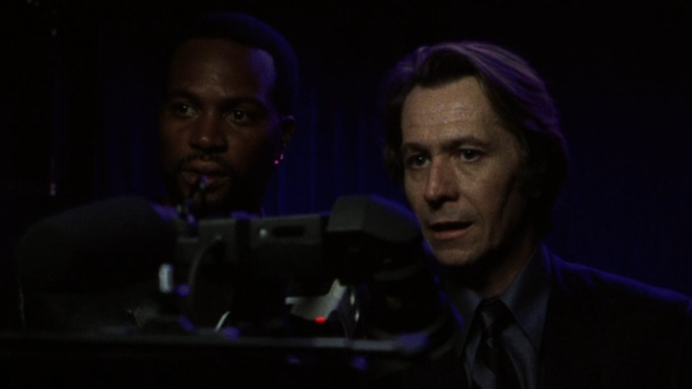 A man and Gary Oldman stand behind a camera