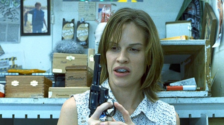 Hilary Swank wearing braces and holding a gun