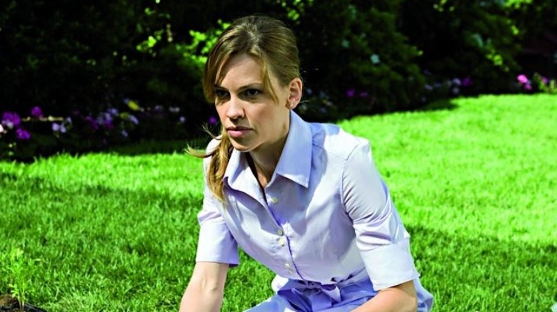 Hilary Swank crouching in a garden