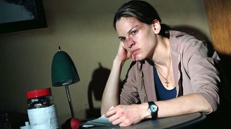 Hilary Swank sitting at a table looking beat up