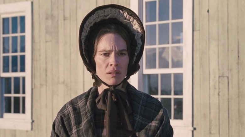 Hilary Swank in a bonnet in front of a barn