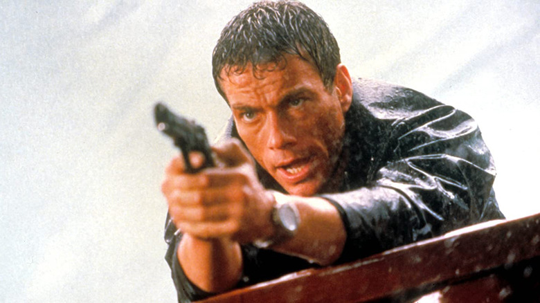 Van Damme aims a gun in the rain