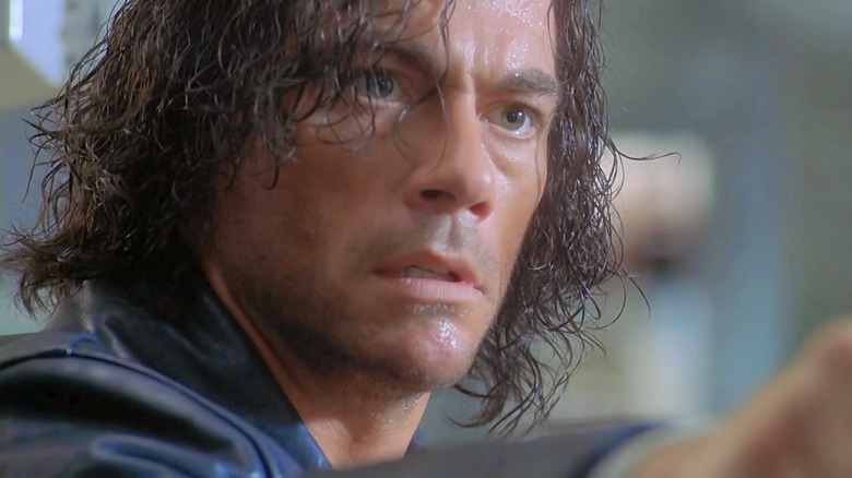 Jean-Claude Van Damme points a gun with a mop of hair