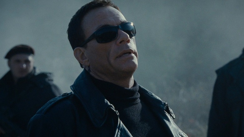 Van Damme in sunglasses backed by henchmen