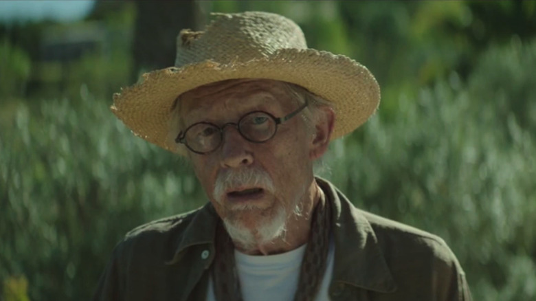 Ralph wears a straw hat in front of bushes