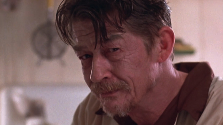 John Hurt leans forward at the table