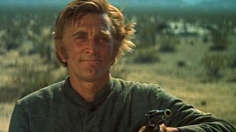 kirk douglas smiles and points a gun