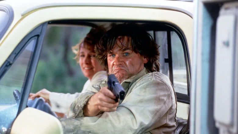 Kurt Russell aims a gun out the window of his car