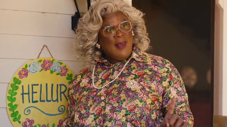 Madea saying hello next to her hellur sign on her porch