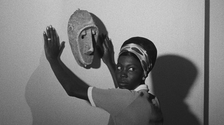 Diouana leans against a wall by an African mask