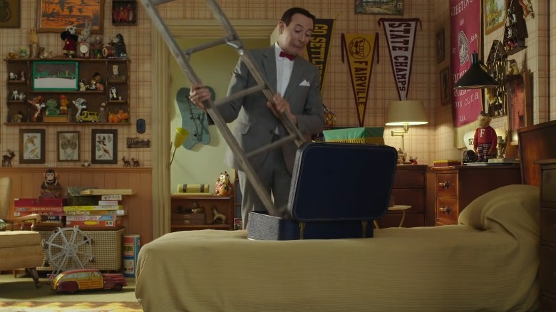 Pee-wee Herman putting an impossibly large ladder into a suitcase