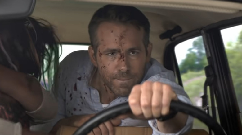A bloody Ryan Reynolds drives a car from the backseat
