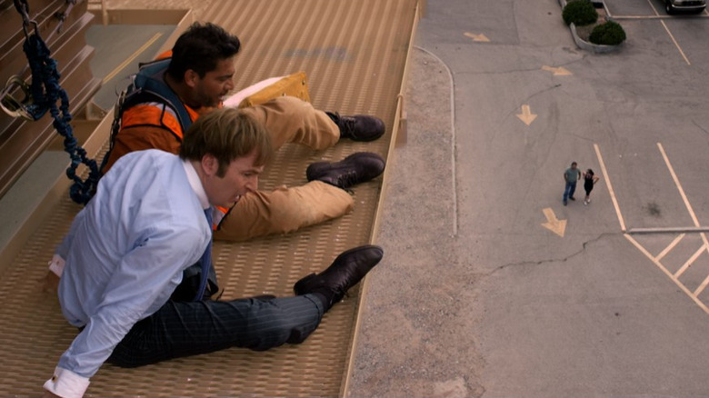 Jimmy and a worker sit on the edge of a billboard 