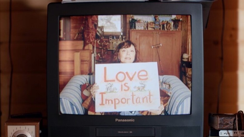 Honey holds up a sign on TV in "Ride the Eagle" (2021)