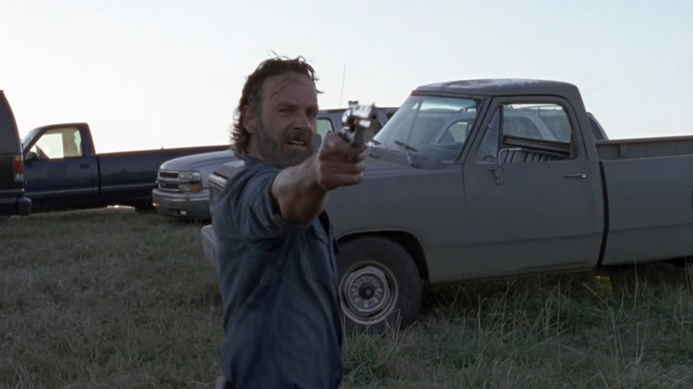 Rick firing gun in front of trucks