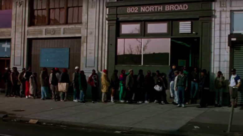 Film still depicting men lined up on sidewalk