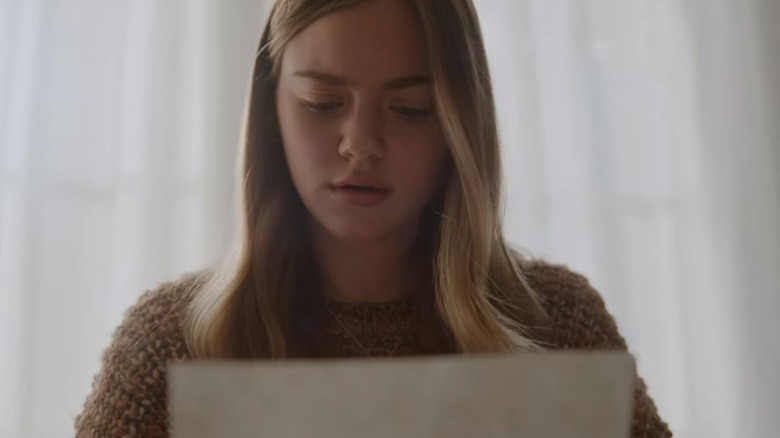 Ellie in a brown sweater, reading a letter