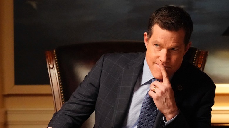 Dylan Walsh sitting at a desk with finger to his lips