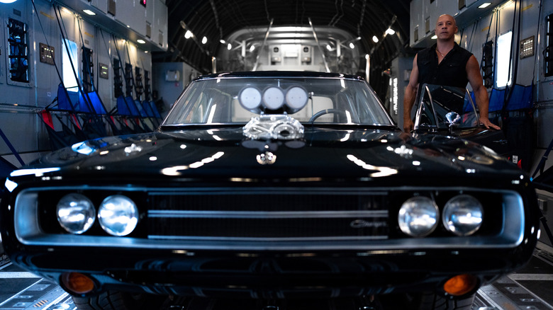 Vin Diesel stands next to a muscle car