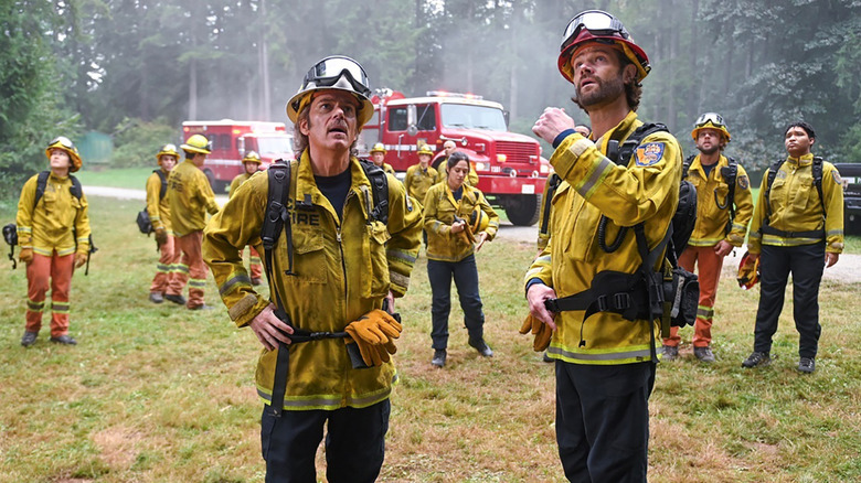 A group of firefighters look up at the sky with concern in 