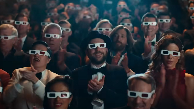 The Fool sits with his publicist in a theater full of people wearing paper 3-D glasses