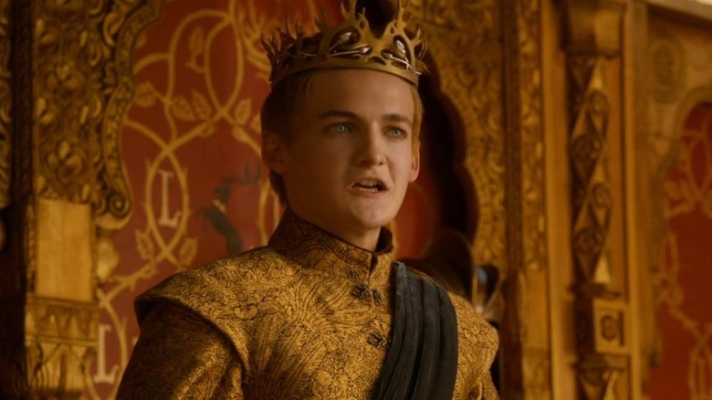 Joffrey Baratheon wearing his crown and speaking in front of a red and gold background