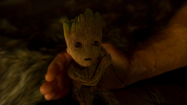 Baby Groot using an earbud while Star-Lord's hand touches him