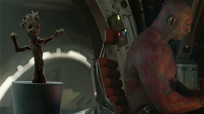 Baby Groot dancing while Drax cleans a knife