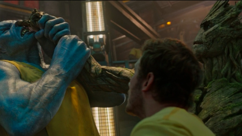 Star-Lord watching while Groot sticks his fingers up an alien's nose