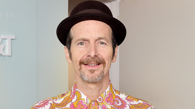 Denis O'Hare, in bright shirt and hat, smiles broadly