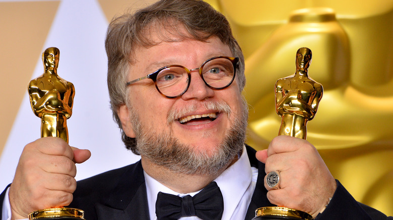 Guillermo del Toro smiling and holding two Academy Awards