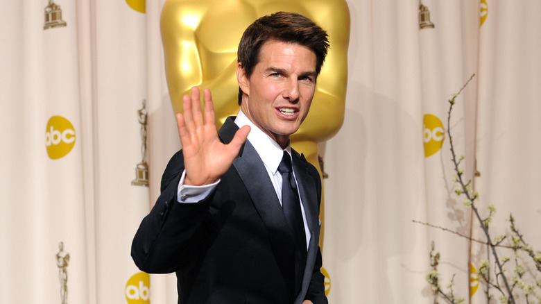 Tom Cruise waving to camera in front of large Oscars statue