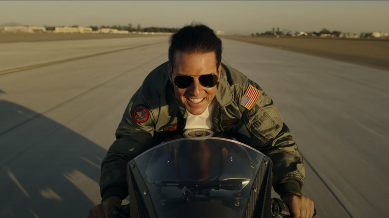 Tom Cruise in Top Gun Maverick smiling while driving a motorycle