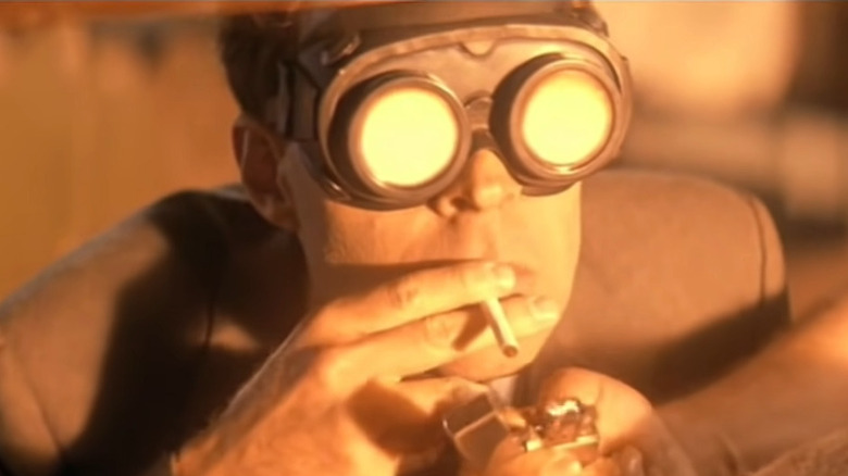 Oppenheimer wears glasses and smokes a cigarette bathed in orange light