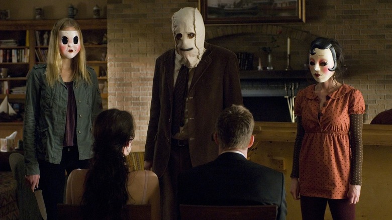 Masked intruders stand over a couple in "The Strangers" (2008)