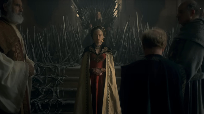 The King sits upon the Iron Throne while his daughter stands before him