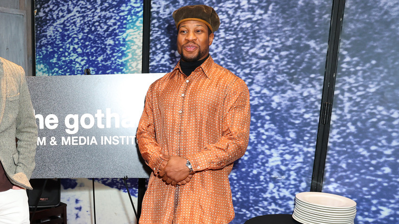 Jonathan Majors smiles by empty plates