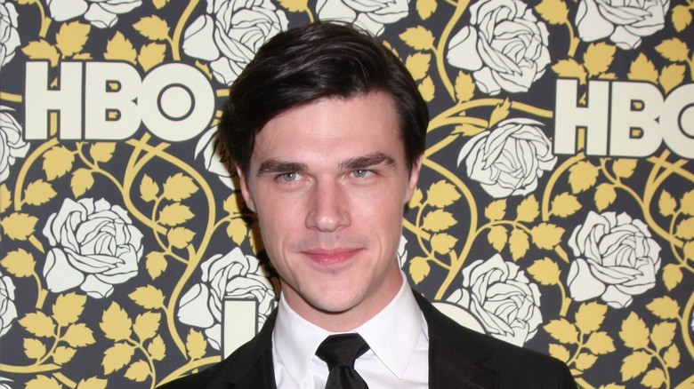 Finn Wittrock standing in front of flower wallpaper wall