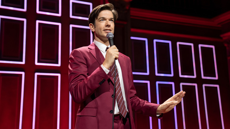 John Mulaney standing on stage and speaking into microphone