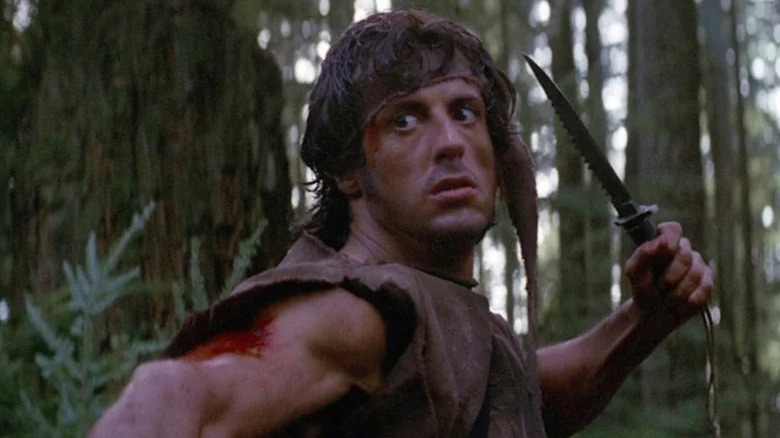 John Rambo in the woods wielding a knife 