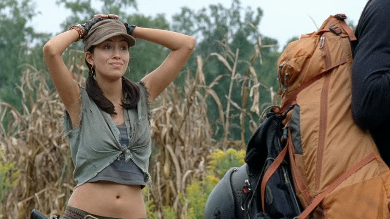 Rosita puts her hands on her head next to a crop field