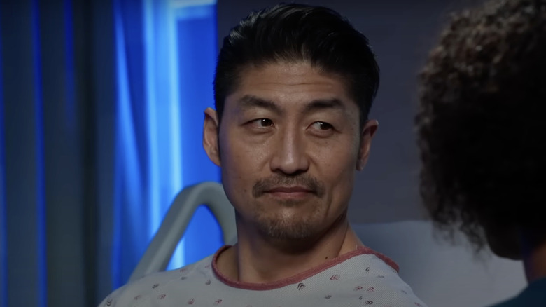 Brian Tee as Dr. Choi wearing hospital gown in bed