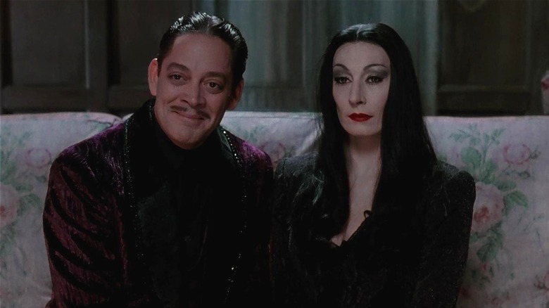 Gomez smiling and Morticia Addams straight-faced while sitting on a couch (1991)