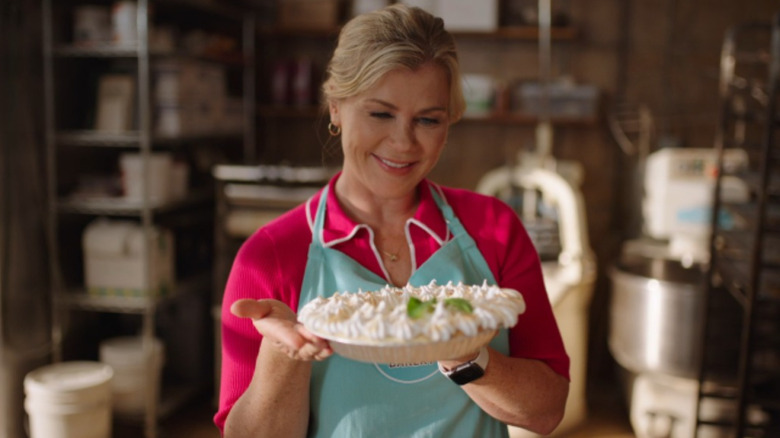 Hannah is standing in a blue apron and holding her lemon meringue pie