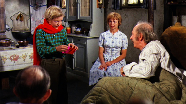 Charlie opens a chocolate bar while his mother and grandfather watch