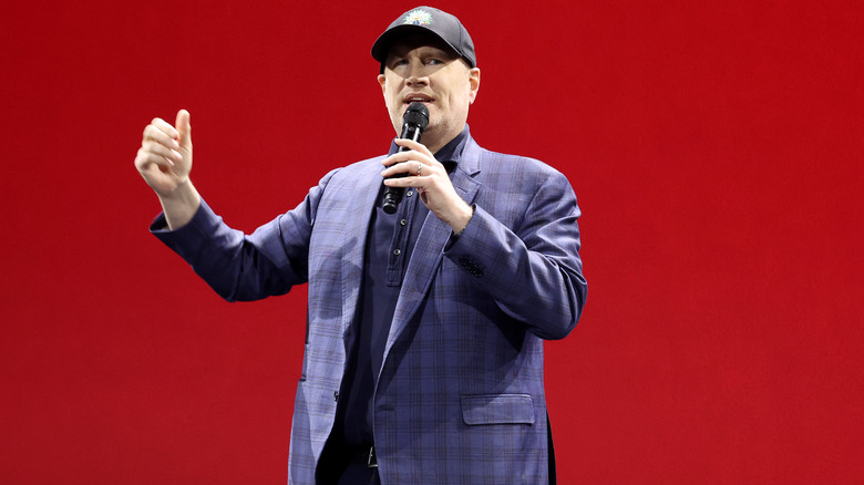 Kevin Feige wearing a baseball cap holding a microphone