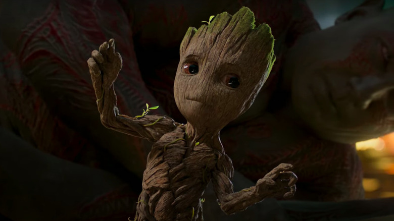 Baby Groot looks at Drax behind it