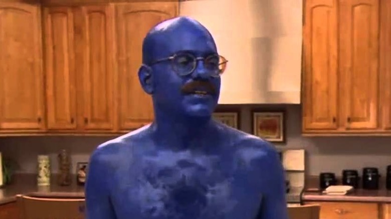 A man painted blue stands in a kitchen