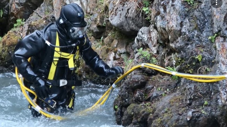 Diver in full-body wet suit standing in river