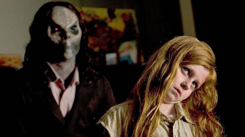 A girl tilts her head with a demon behind her in Sinister